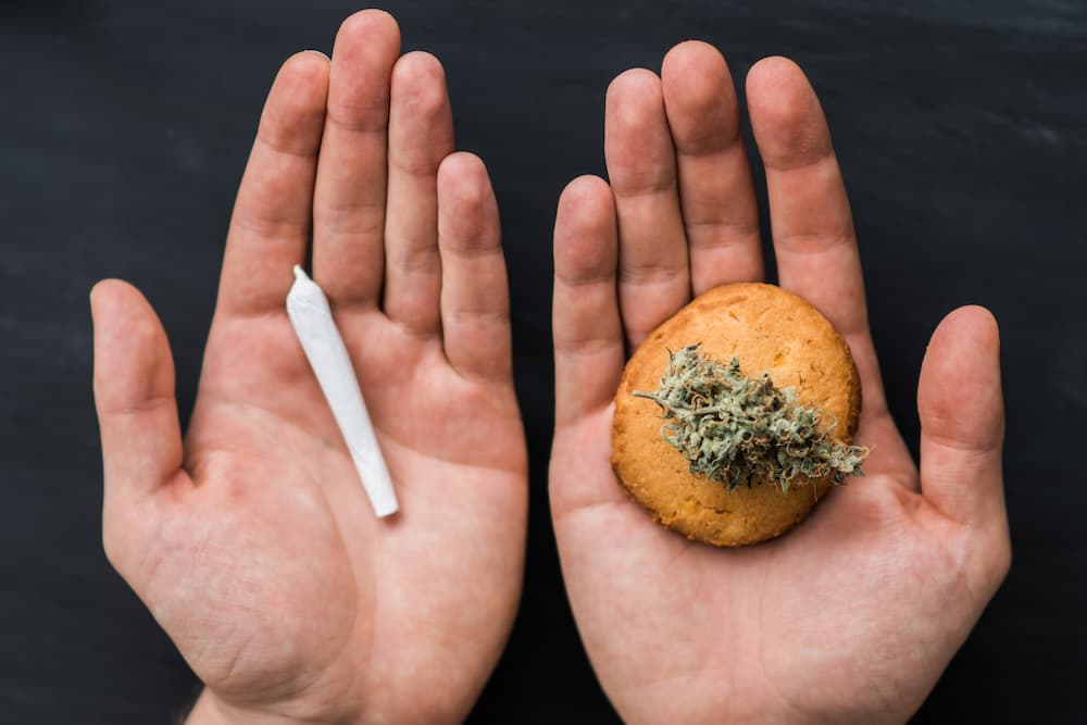 Hands holding a rolled joint and a cookie with cannabis flower laying on it